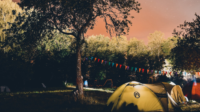 Campingplatz mit erleuchteten Zelten und Wimpelkette zwischen Laubbäumen.